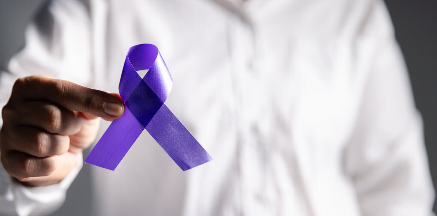 Pessoa segurando um laço roxo, símbolo da campanha Maio Roxo, que promove a conscientização sobre doenças inflamatórias intestinais como Crohn e retocolite ulcerativa.